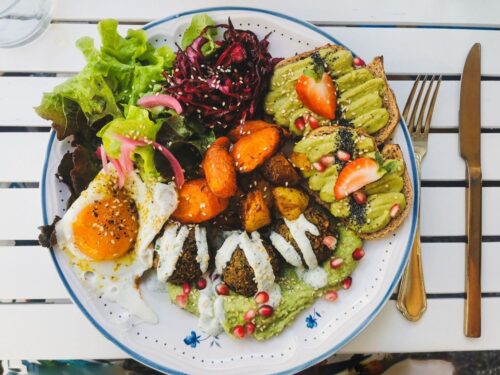 Fargerik frokosttallerken med avokadotoast, egg, salat og ovnsbakte grønnsaker